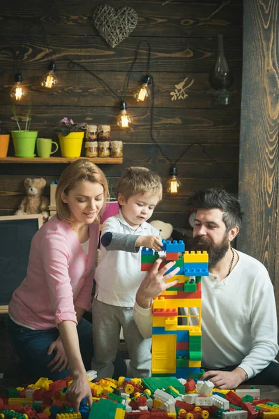 Family spend time together in playroom. Parents help cute son to make a house out of plastic blocks. Daddy supporting construction and mom choosing pieces while their kid builds a tower — Stock Photo, Image