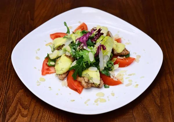 Sallad serveras i vit platta, mörk trä bakgrund. Maträtt restaurangkoncept. Skålen i restaurang - sallad med tomater, ruccola, sallad, ost, mandel marker, radicchio, stekt kött. — Stockfoto