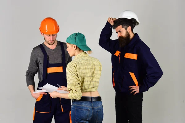 Brigade de travailleurs, constructeurs de casques, réparateurs et dame discutant contrat, fond gris. Concept de recrutement. Brigadier, contremaître embauchant des travailleurs pour réparation, signe un contrat . — Photo