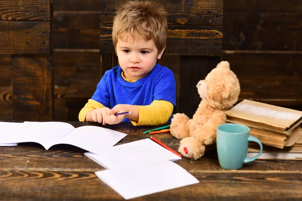 Torniamo a scuola. Il ragazzo sta guardando dei quaderni su un tavolo di legno. Piccolo ragazzo concentrato che tiene matite colorate — Foto Stock