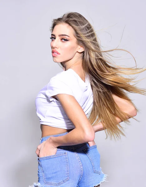 Conceito de cuidados com o cabelo. Senhora sexy com cabelo brilhante saudável. Menina com cabelos longos usa shorts jeans curtos, fundo claro. Mulher atraente no rosto calmo desfrutando de seu cabelo acenando no ar . — Fotografia de Stock