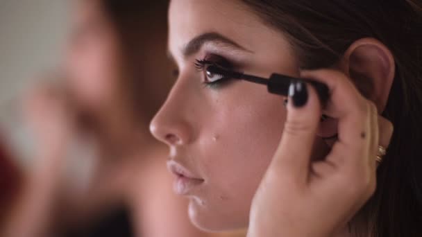 化妆艺术家应用睫毛膏模型 关门了化妆师为女孩在室内化妆 化妆师在模特眼中应用鲜艳的基色眼影 — 图库视频影像