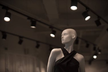 Manken giyimleri şık avizeler ile gri arka plan üzerinde içinde. Alışveriş ve butik konsept. Şık lüks bebek parlayan. Siyah elbise ile beyaz plastik manken.