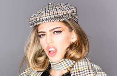 Kadını ile utanmış yüzündeki damalı aksesuarları ile yapın. Uzun saçlı kız giyer ekose kepi, eşarp, gri arka plan. Şık kıyafet, seksi Bayan kapatın. Moda aksesuarları kavramı.