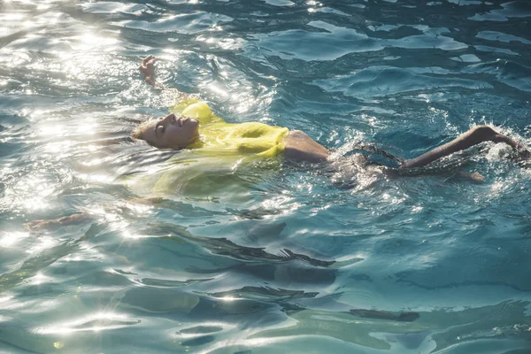 Schöne junge Frau im sexy gelben Kleid schwimmt am Meeresstrand — Stockfoto