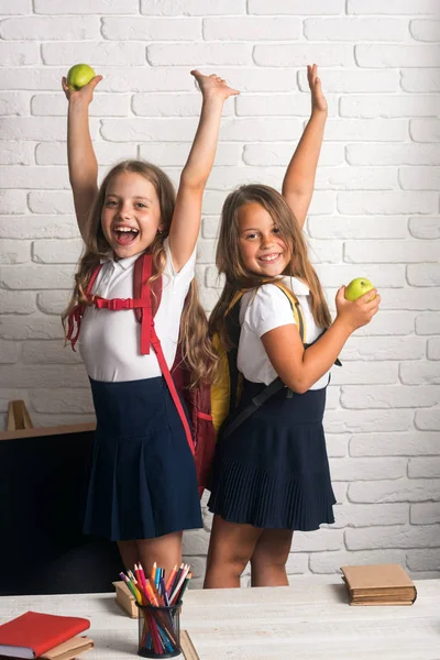 Kleine meisjes eet appel bij de lunchpauze. Terug naar school en huis het scholen. Gelukkig schoolkinderen op les in 1 september. Vriendschap van kleine zusters in de klas op de dag van de kennis. Schooltijd van meisjes — Stockfoto