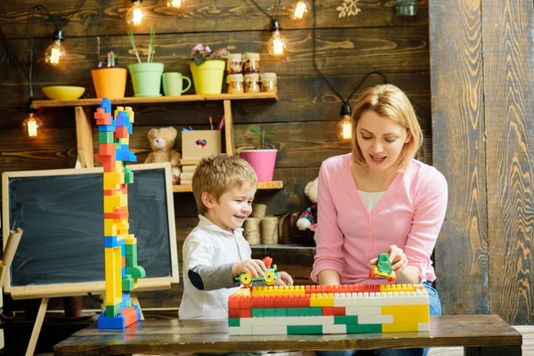 Madre e hijo juegan con bloques constructores. Mamá y el niño compitiendo con coches de plástico. Mamá hablando con su hijo mientras sostiene el tren de juguete. Guardería con pizarra sobre fondo — Foto de Stock