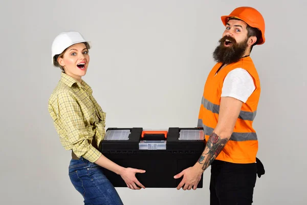Repairman and girlfriend holding toolbox together, copy space. Smiling woman in helmet excited about renovation. Builders with toolbox, couple in love makes repair grey background. Renovation concept. — Stock Photo, Image