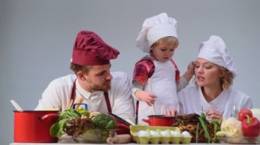 Sevimli küçük bir çocuk ve onun güzel anne mutfakta yemek yaparken gülümsüyorsun. Genç aile yemek yemek mutfakta. Mutlu bir aile birlikte yemek. Mutlu genç ailesi ile anne, baba çocuk yemek.