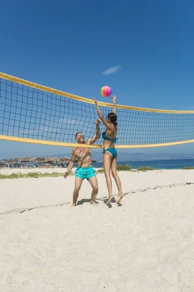 Young sporty active couple beat off volley ball, play game on summer day. Woman and man fit, strong, healthy, doing sport on beach. Beach volleyball concept. Couple have fun playing volleyball.