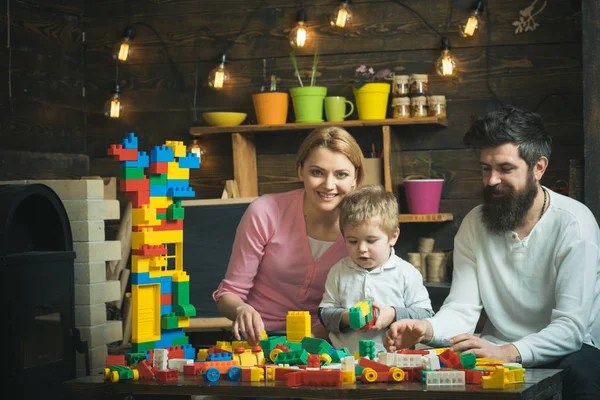 Familia disfrutando del tiempo juntos. Papá e hijo jugando con bloques de plástico. Padre, madre y su lindo hijo sentados alrededor de la mesa con ladrillos de construcción de colores —  Fotos de Stock