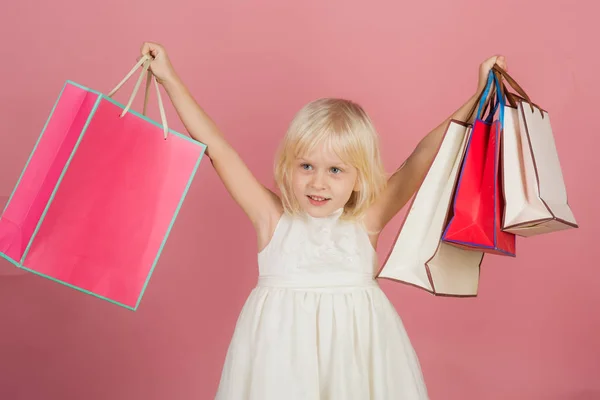 Una chica pequeña va de compras. Sonrisa infantil con bolsas de papel en la tienda. Chico de moda y belleza mirada. Celebración y fiesta de cumpleaños. tendencia pastel picante. venta en viernes negro o lunes cibernético . —  Fotos de Stock