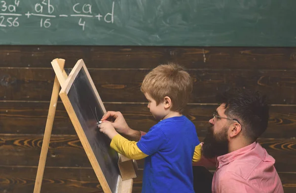 Studente vista laterale e insegnante di fronte alla lavagna. Padre o tutor aiutano il bambino a scrivere lettere. Uomo e bambino su pannelli di legno sfondo — Foto Stock