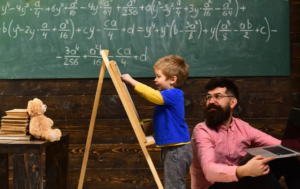 Piccolo studente con insegnante sorridente in classe. Vista laterale adorabile bambino che scrive sulla lavagna. Concetto di apprendimento precoce — Foto Stock