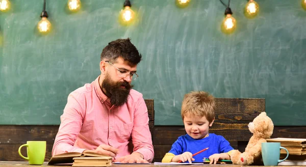 先生は、小さな子供のコピーブックに手紙を書きます。かわいい男の子がカラフルな鉛筆で絵を描きます。幼稚園アート レッスン — ストック写真