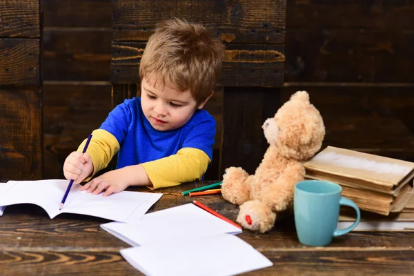 Koncentrovaná kreslení linie chlapec s modrou tužkou. Zaneprázdněný, co píše v knize cvičení. Žák na dřevěné panely pozadí — Stock fotografie