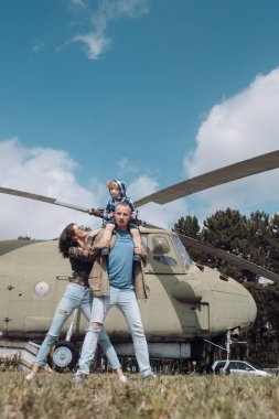 Mutlu aile zaman harcamak birlikte, gezi, arka plan, helikopter üzerinde güneşli bir gün. Aile Eğlence kavramı. Anne ve baba ve Havacılık Müzesi havada yürüyüş çocuk. Baba oğul boynunda taşır..