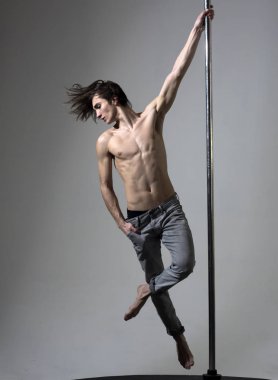 Kutup dans performans sporcu atlet, hamle, iş dışarı, numara göstermek. Spor ve sanat kavramı. Çekici, seksi adam uzun saçlı, çıplak gövde, gri arka plan. Adam rakam kutubun, gösterir hile yapıyor.