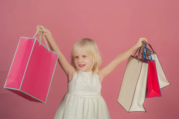 Celebración y fiesta de cumpleaños. Una chica pequeña va de compras. Sonrisa infantil con bolsas de papel en la tienda. Chico de moda y belleza mirada. tendencia pastel picante. venta en viernes negro o lunes cibernético . —  Fotos de Stock