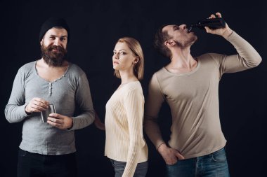 Çocuklar tutun Kupası, şişesi ile alkol, içki. Sakin arkadaş şirket içecekler ile boş zaman harcamak. İçki alkol kavramı. Alkol, arkadaşlık, eğlence. Erkek, kadın dalgın yüzleri, koyu arka plan.