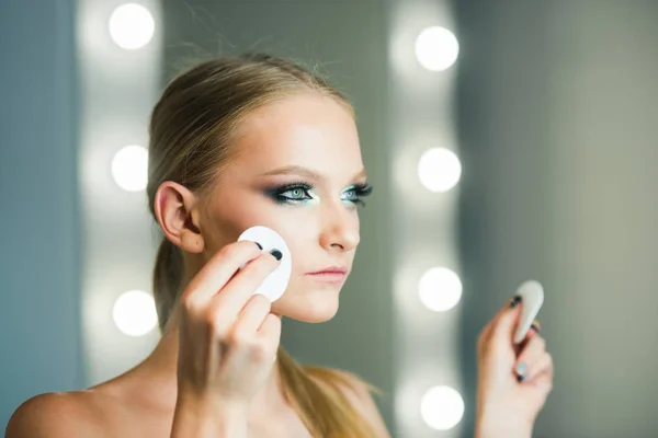 Woman using cotton pad on face for makeup removal.