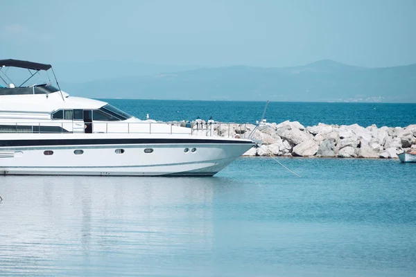 Barco de alta velocidade, iate de luxo na doca no mar, céu azul no fundo. Iate de luxo branco, planadores marinhos na superfície do mar. Navio moderno e caro perto de quebra-mar rochoso. Conceito de cruzeiro e turismo . — Fotografia de Stock