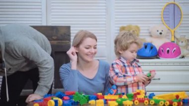Genç aile inşaat plastik blokları ile oyun oynamak. Aile Oyunları kavramı. Anne ve çocuk mutlu yüzler ile kırmızı tuğla tutun. Baba, anne ve oğlu ışık ahşap arka plan üzerinde oyun odası.