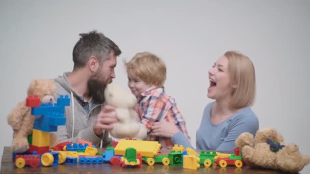 年轻家庭玩游戏与建筑塑料块 家庭游戏的概念 父母和孩子带着快乐的面孔 拿着红砖 母亲和儿子在游戏室中轻木背景 — 图库视频影像