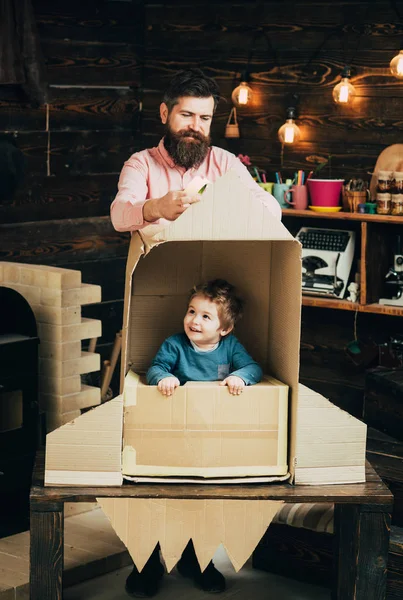 Kid happy sit in cardboard hand made rocket. Parenthood concept. Boy play with dad, father, little cosmonaut sit in rocket made out of cardboard box. Child boy play cosmonaut, astronaut.