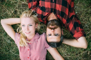 Romantik Çift parkta çim üzerinde yalan. Sarışın kadın ve sakallı adam bükülmüş kollar ve eller başlarını altında ile rahatlatıcı yukarıdan görüntüleyin. Yaz tatil romantik.