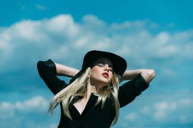 Genç kadın mavi gökyüzü arka plan üzerinde poz karanlık şapkalı.