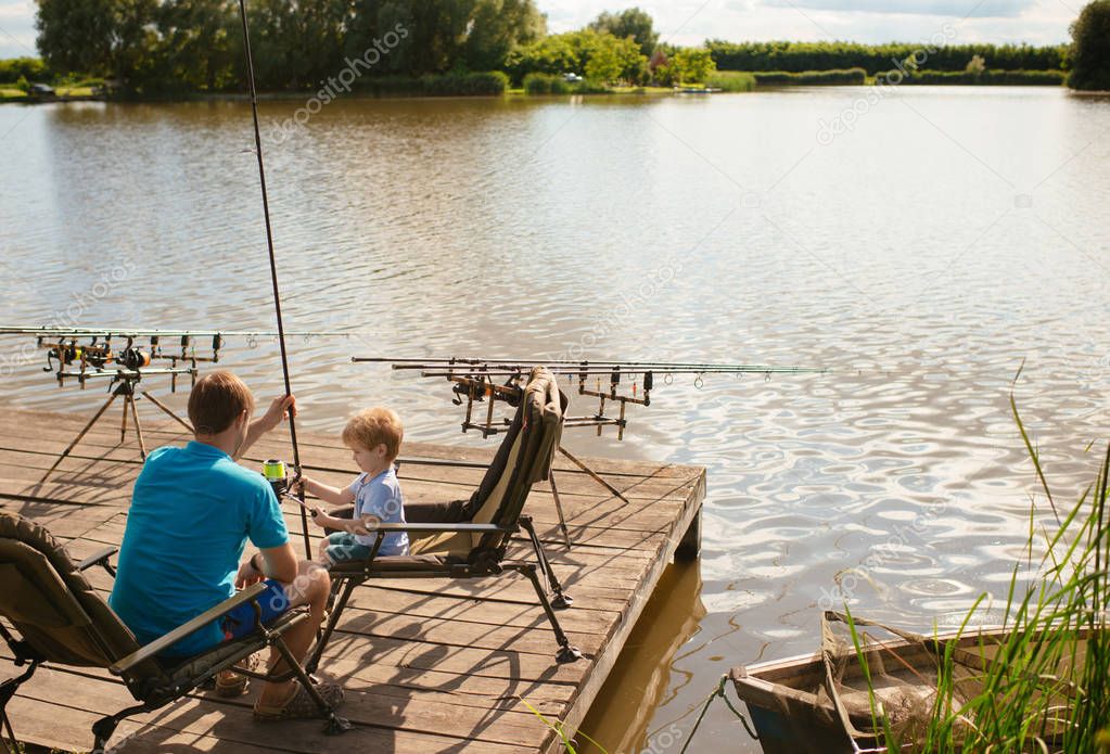 Father teaching son to fish sitting at lakeside