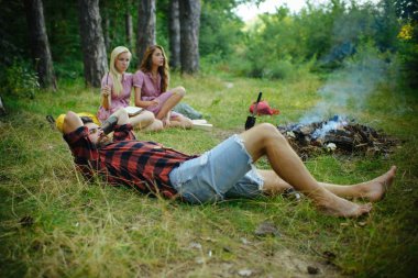 Gökyüzü, doğa kavramı ile birlik bakarak ve çim üzerinde yalan oduncu gömlekli sakallı adam. Ormanda kamp arkadaş grubu.