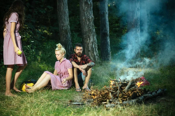 妇女和男子在营地火灾的老式风格 朋友们在篝火旁放松 人们在篝火圣火在绿色森林 远足和旅行 暑假概念 — 图库照片