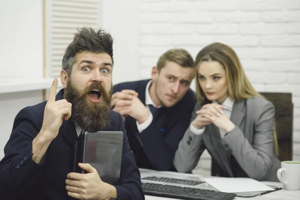 Man with beard on surprised face holds laptop, bosses, coworkers, colleagues on background. Man got job, successful meeting. Man surprised, hired for work in office. Successful job interview concept.