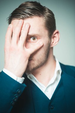 Adam korkmuş bakışla yüzünü eli ile gizleme portresi. Sakallı adam gri arka plan üzerinde izole spread parmakları bakarak.