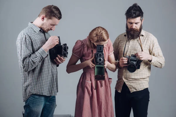 Vintage photography concept. Men in checkered clothes, retro style. Company of busy photographers with old cameras, filming, working. Men and woman on pensive faces on grey background.