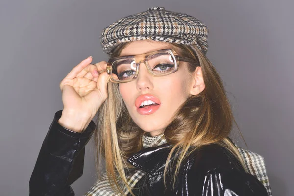 Woman on pensive face with make up wears checkered accessories and glasses for vision. Accessories concept. Girl wears kepi, scarf and glasses, grey background. Sexy lady in stylish outfit, close up.