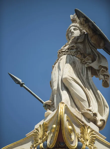 Statue, sculpture of Greek warrior in helmet with spear and shield. White sculpture ancient greek god of war with gilding. Statue of man in armor with blue sky on background.