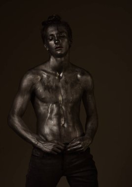 Moda ve erotik bir kavram. Adam kendine güvenen seksi ifade ile poz. Adam çıplak gövde ile parıldayan gümüş boya, koyu arka plan ile kaplı. Maço akışları ter veya çıplak göğüs üzerinde boya ile.