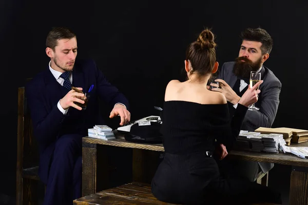 Men and woman sitting at table with piles of money. Illegal deal concept. Businessmen discussing illegal deal while drinking and smoking, dark interior background. Company engaged in illegal business.