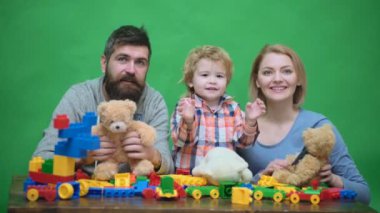 Genç aile inşaat plastik blokları ile oyun oynamak. Aile Oyunları kavramı. Anne ve çocuk mutlu yüzler ile kırmızı tuğla tutun. Baba, anne ve oğlu ışık ahşap arka plan üzerinde oyun odası.