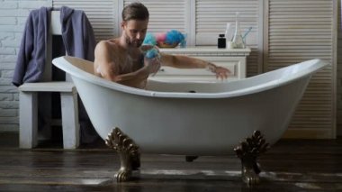 Yakışıklı delikanlı rahatlatıcı küvette. Beyaz bir buthtub banyoda sakallı adam. Erkekler köpük köpük banyosu lüks küvet içinde mutluluk ve rahatlatıcı ile kaplı.