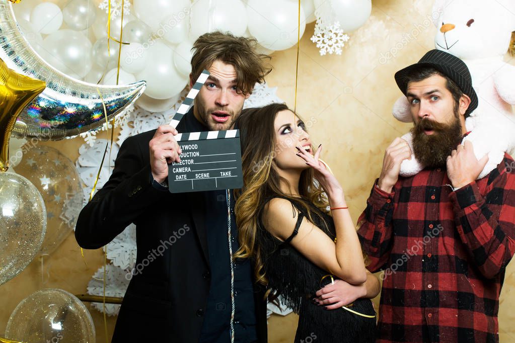 Lovers celebrate christmas or new year, love triangle. Boyfriends with movie clapper and teddy bear toy. Sensual woman and men in movie or film studio. Cinema theme party for holiday celebration.