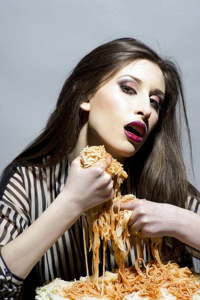 Food, diet and cuisine. Sexy woman eat spaghetti with hands. Woman eat pasta dish with tomato ketchup. Hungry girl have italian food meal. Beauty model with makeup and long brunette hair have dinner.