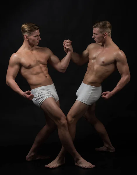 Twins men with muscular body in balance pose. twins muscular men in bodybuilder pose isolated on black background