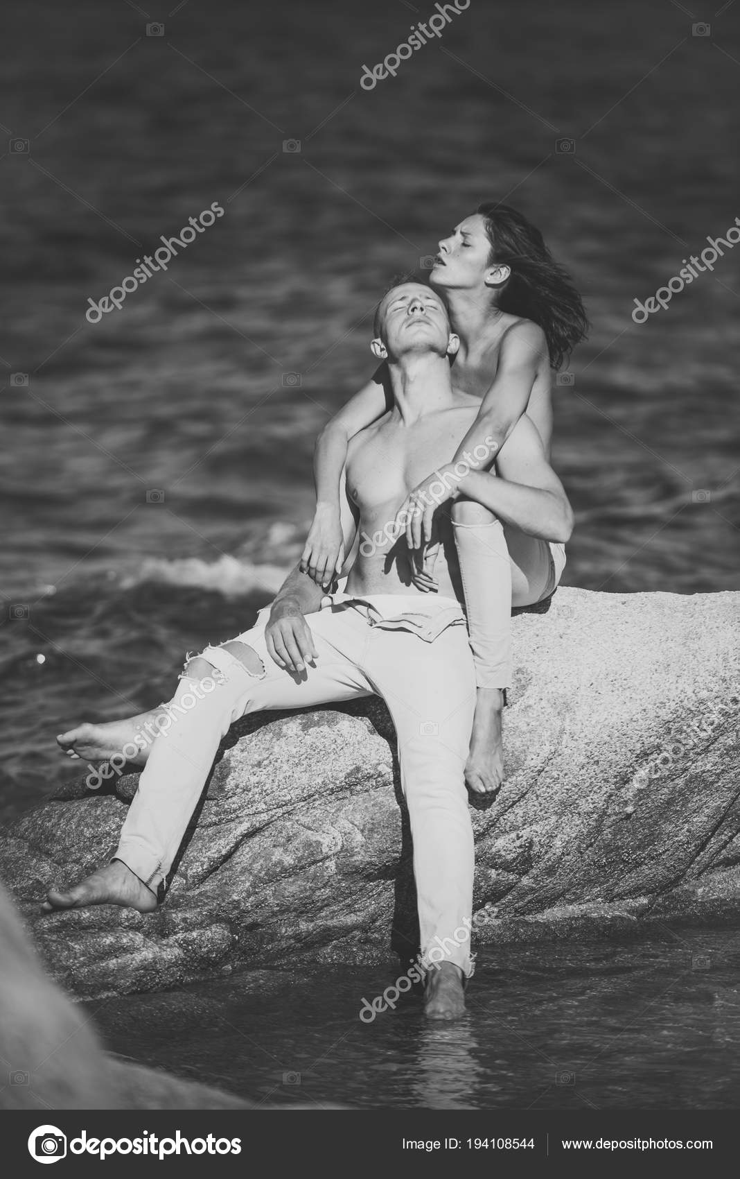 Nudist family photos happy Sexy topless couple sits on stone or reef in sea. Happy family spend time  together, hugs