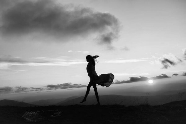 Woman or girl silhouette walking at beautiful view on sunset or sunrise in blue sky with clouds and yellow orange sun in mountains on natural background