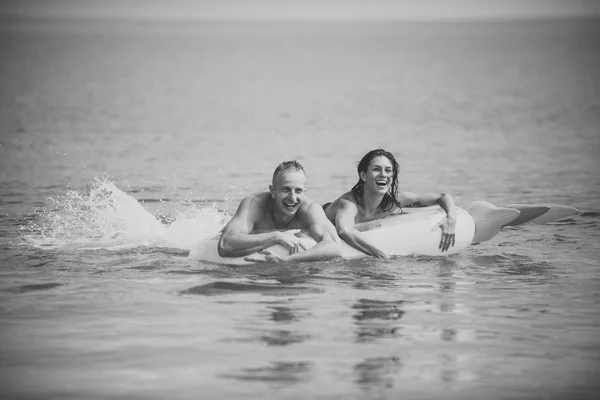Happy young couple swimming and laughing on air mattress. Couple vacation concept. Man and woman on honeymoon, swim on pineapple shaped mattress in sea. Summer accessories for rest yellow air mattress