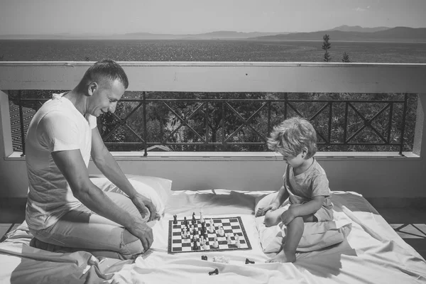 Concept intelligent pour tout-petit. Papa avec enfant jouer jeu intellectuel. Parent jouer aux échecs avec l'enfant sur la terrasse par une journée ensoleillée. Père et petit fils jouent aux échecs sur le balcon, la nature et la mer sur fond . — Photo